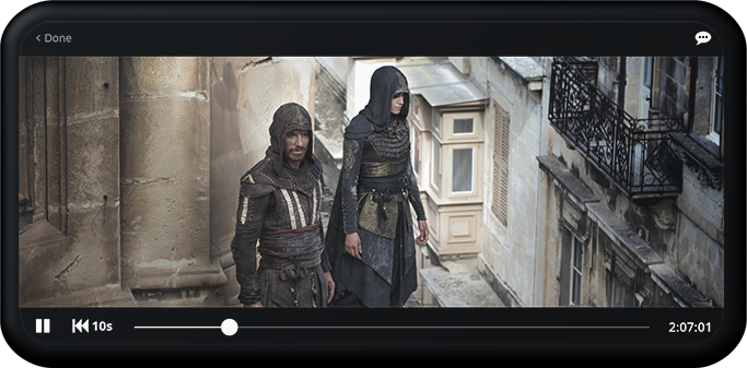 Two individuals dressed in medieval-style costumes walking along a stone balcony with ornate architecture.