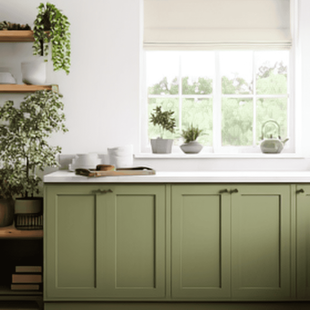 Bright kitchen with green cabinets and potted plants by window.