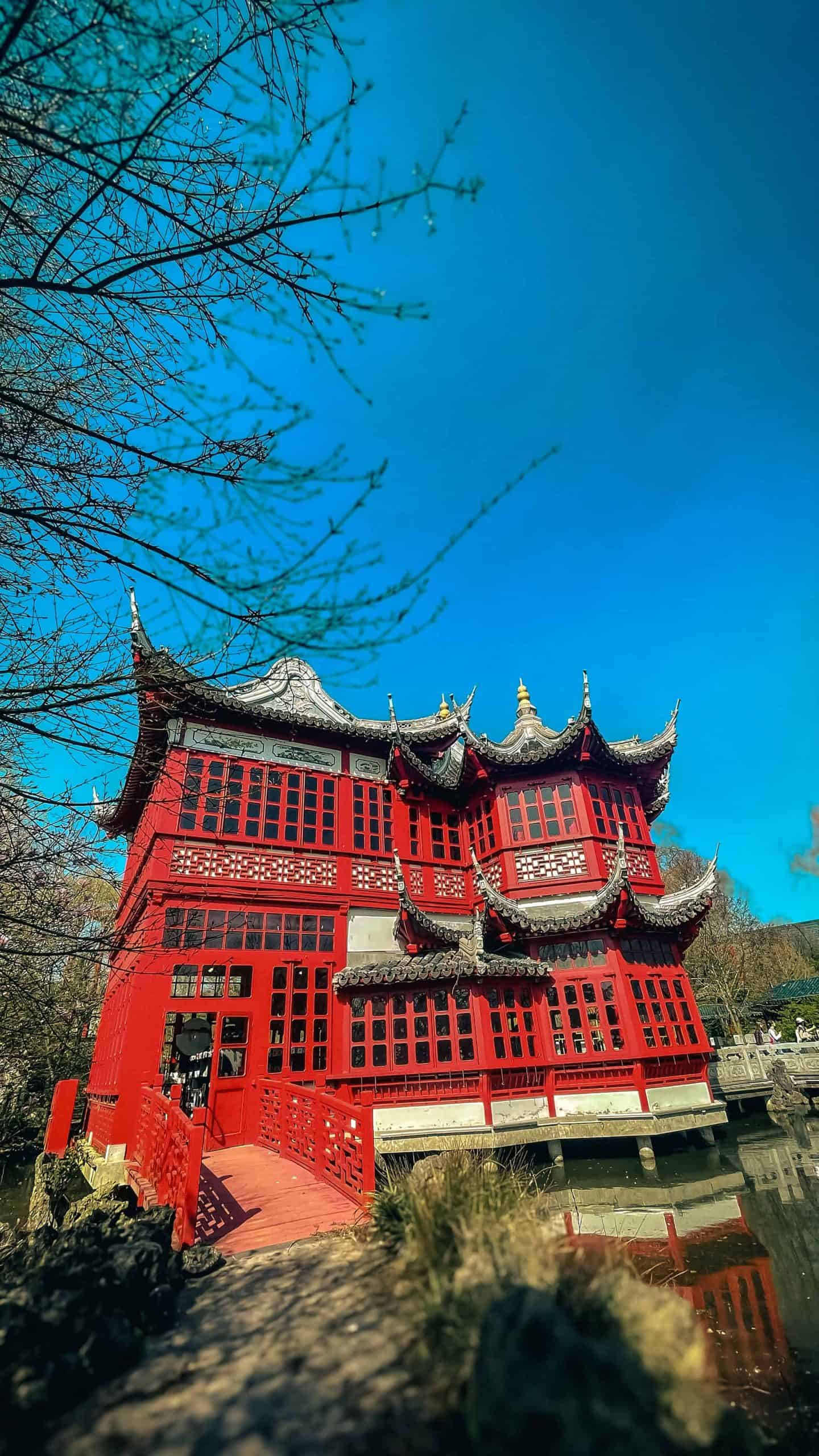 Traditional Chinese pagoda with red walls and ornate roof details in a garden setting.
