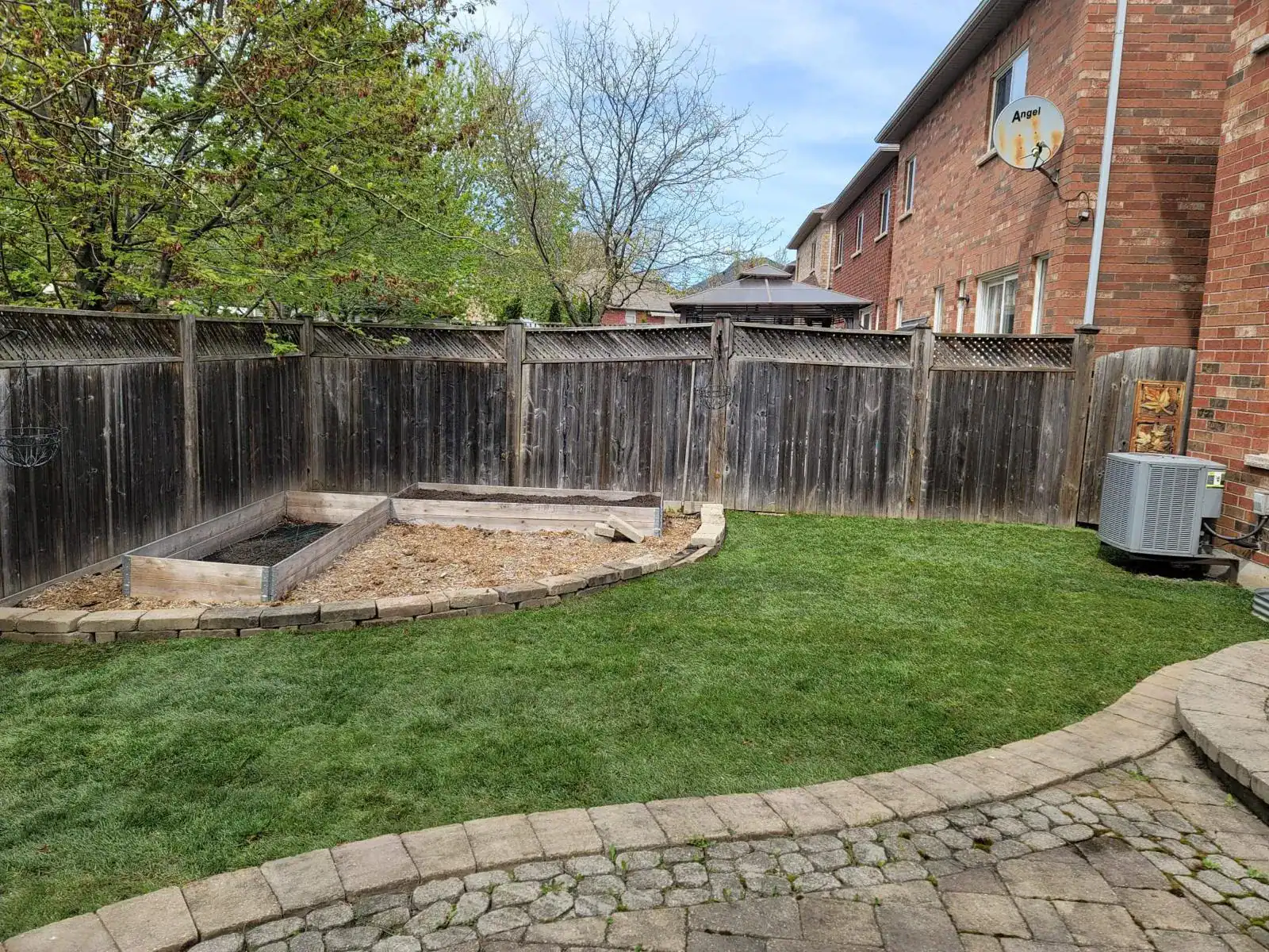 Lush green backyard with new sod, raised garden beds, and a paved stone patio.