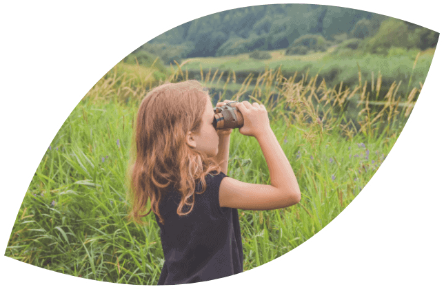 La foto raffigura una bambina che sta guardando in un binocolo in un ambiente naturale vuole raffigurare NET un progetto che guarda al lontano