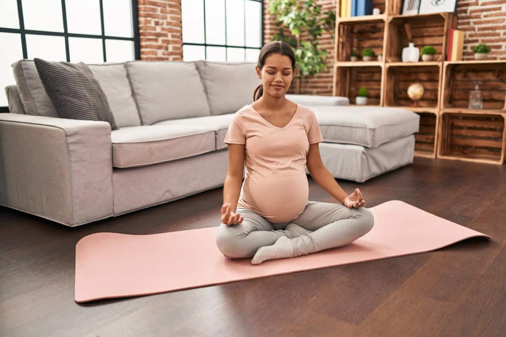 Pregnant woman practicing meditation in a cozy living room environment.