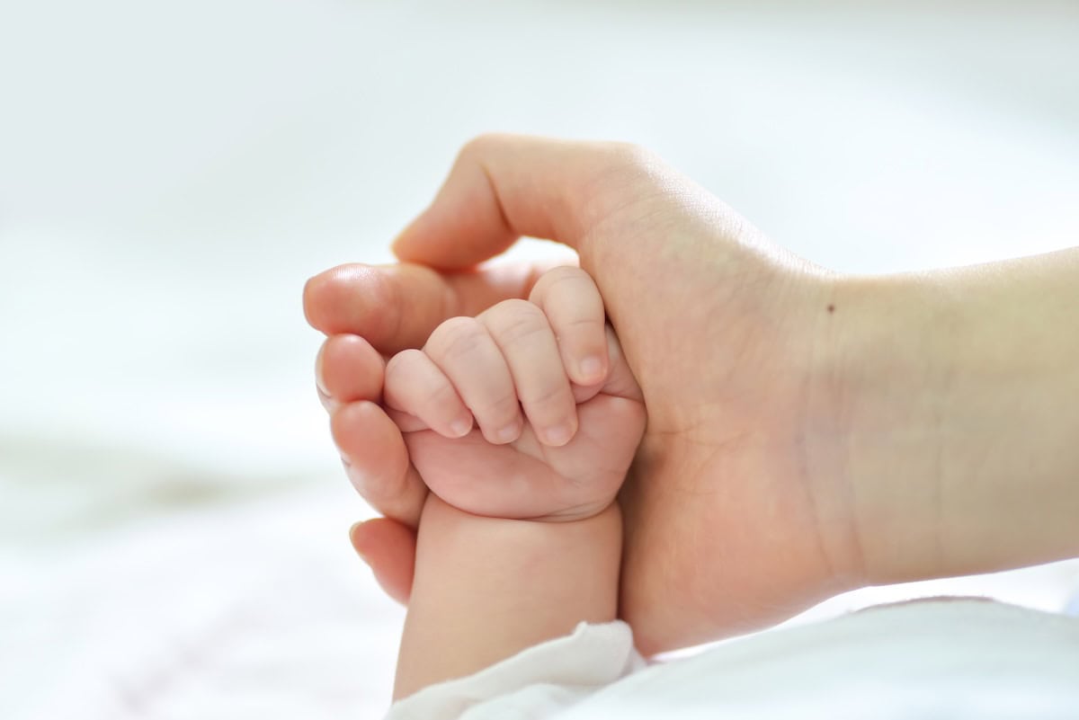 Close-up of an adult hand holding a baby's hand for fertility care.