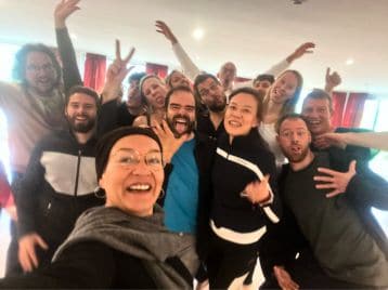 Eine Gruppe von Menschen posiert eng beieinander in einem Raum, lächelt und macht spielerische Gesten in Richtung Kamera, um ihre NLP-Ausbildung und ihren Sinn für Mitgliedschaft zu feiern.