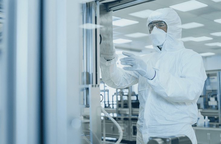 Technician in a full cleanroom suit and mask adjusting or inspecting equipment inside a sterile laboratory or manufacturing environment.