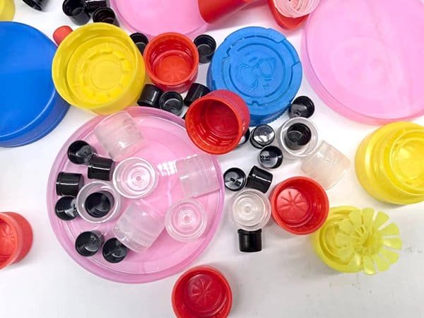 Multicoloured plastic bottle caps and lids scattered on a white surface, emphasizing recycling, waste reduction, and eco-friendly packaging solutions for sustainable business practices.