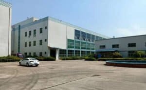 Modern office building with glass windows and parking lot in an industrial area during daytime.