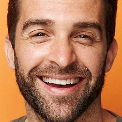 Bright smiling man with a beard, close-up portrait, cheerful expression, warm background, conveying positivity and confidence for financial or investment branding.