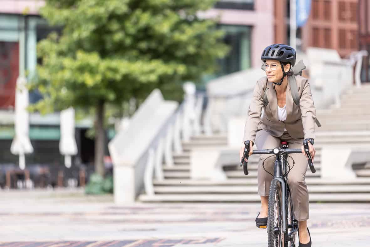Frau trägt Helm und fährt Fahrrad in urbaner Umgebung.