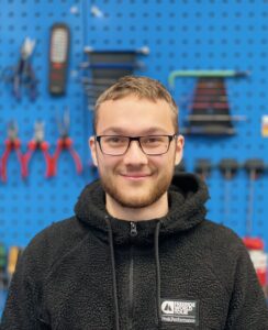 Rad & Tat Tübingen - Werkstattservice Junger Mann mit Brille vor Werkzeugwand in Werkstatt.