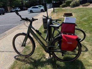 Electric bicycle with red delivery bags parked on grass near parking lot.