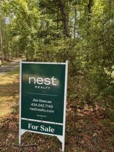 Real estate sign for Nest Realty in a wooded area.