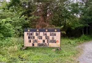 Motivational sign in a wooded area with greenery and a dirt path.