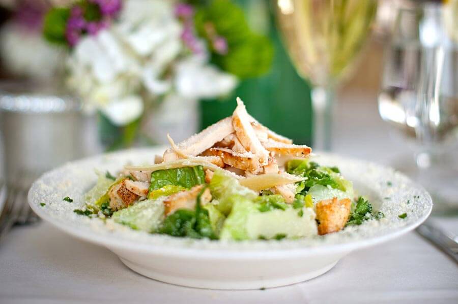 Chicken Caesar salad with romaine lettuce, croutons, and shaved parmesan cheese, served in a shallow white bowl.