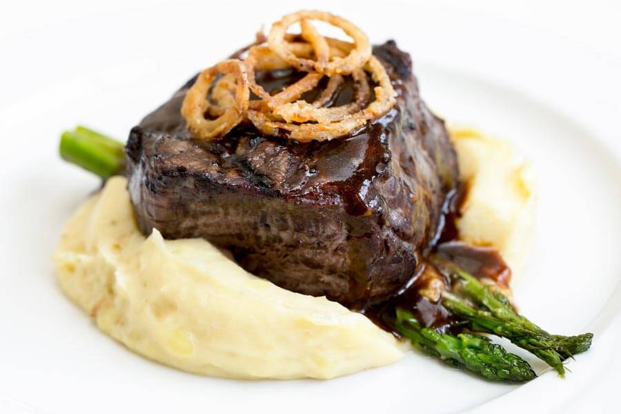 Grilled steak over mashed potatoes and asparagus, topped with gravy and fried onion rings.