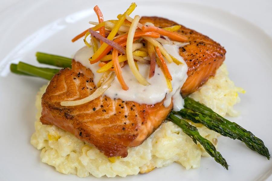 Pan-seared salmon over risotto with asparagus, cream sauce, and julienned vegetables.