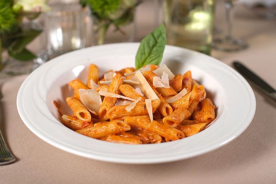 Penne pasta in tomato sauce topped with shaved parmesan cheese and a fresh basil leaf.