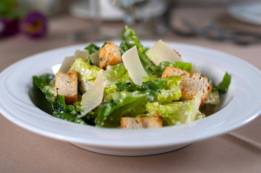 Caesar salad with romaine lettuce, croutons, and shaved parmesan cheese in a white bowl.