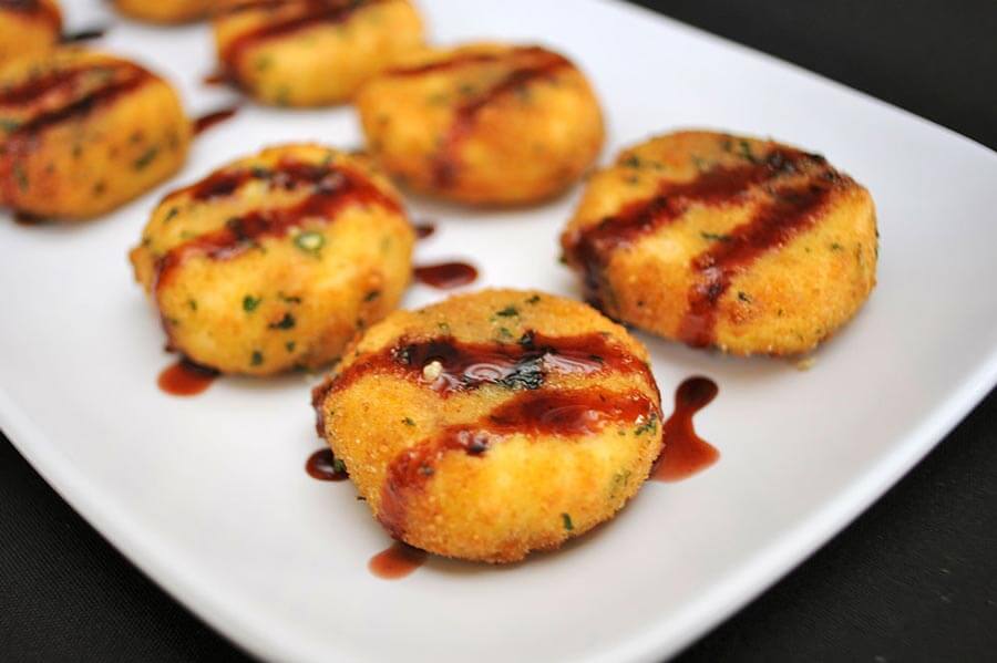 Pan-fried potato cakes or fritters drizzled with a dark savory sauce, served on a white platter.