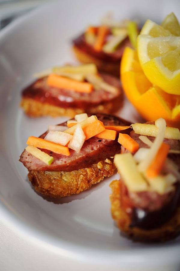 Sausage appetizers on toasted bread topped with chopped vegetables, served next to fresh citrus.