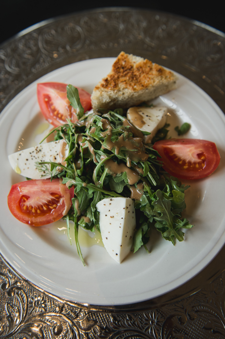 Caprese salad with fresh mozzarella wedges, sliced tomatoes, and arugula, served with a side of bread.
