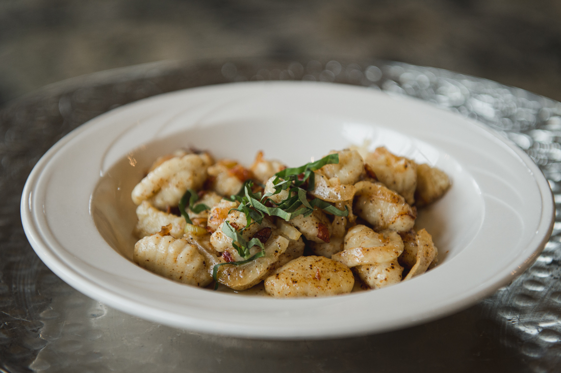 Gnocchi pasta tossed with caramelized onions and herbs, served in a white bowl.