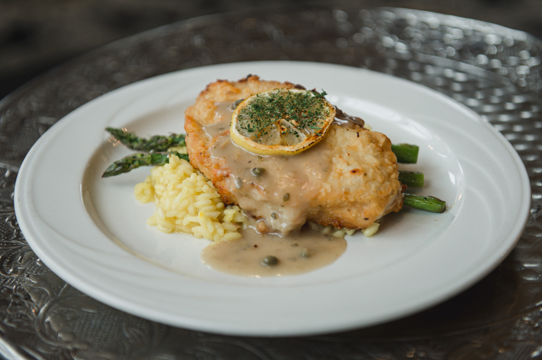 Chicken piccata with a lemon slice and caper sauce, served over risotto and asparagus.