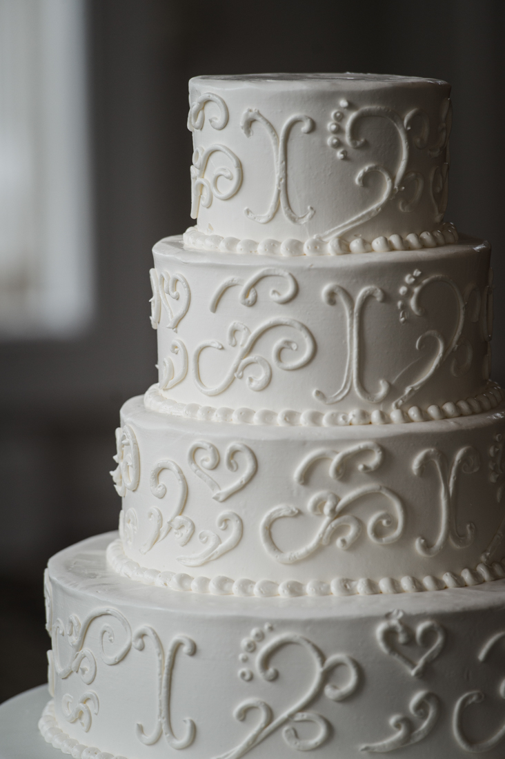 Four-tier white wedding cake decorated with elegant buttercream piping and scrollwork.