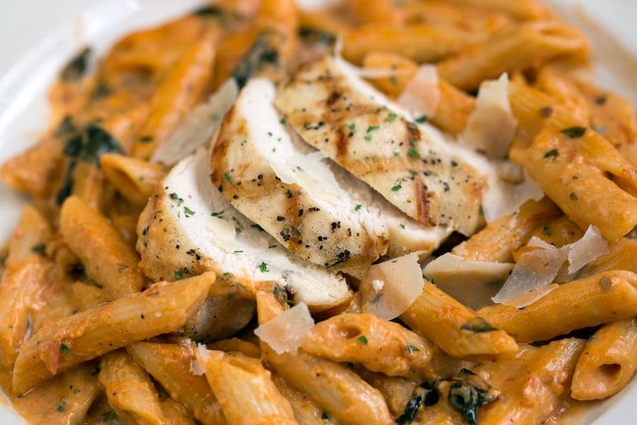 Sliced grilled chicken breast over penne pasta in tomato cream sauce, topped with shaved cheese.