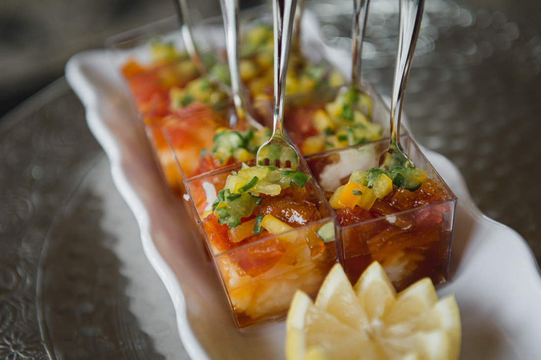 Individual seafood or shrimp cocktail appetizers served in clear mini cups with forks, topped with diced mango salsa, arranged on a white platter.