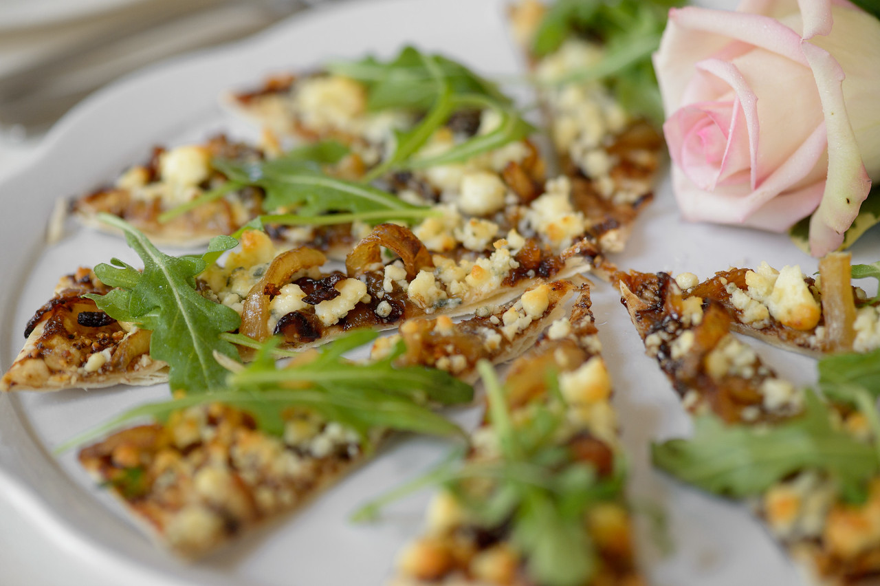 Slices of flatbread with caramelized onions, goat cheese, and fresh arugula next to a pink rose.