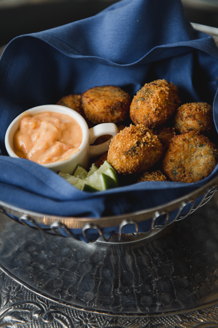 Fried croquettes in a blue-lined basket served with lime wedges and a creamy dipping sauce.