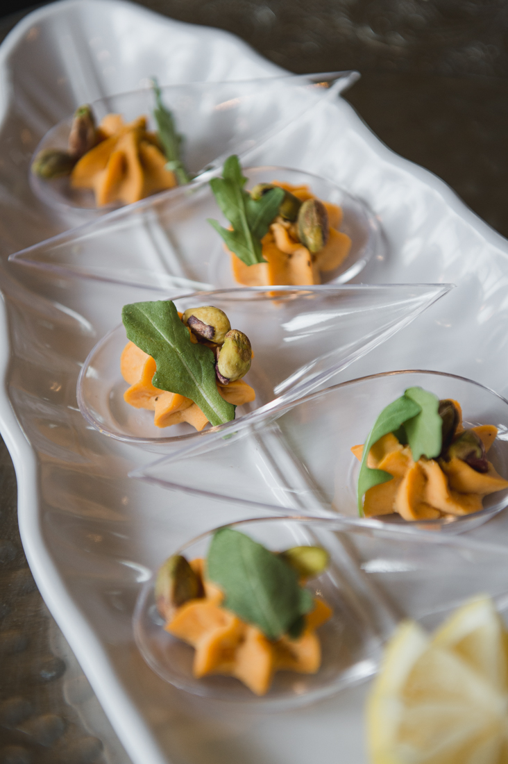 Piped orange mousse appetizers in teardrop spoons topped with pistachios and a green leaf.