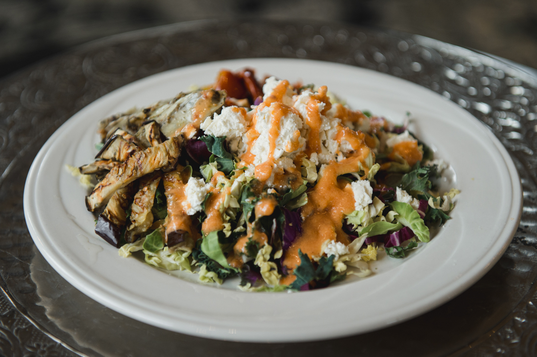 Mixed greens salad with grilled eggplant, crumbled feta cheese, and an orange dressing served on a white plate.