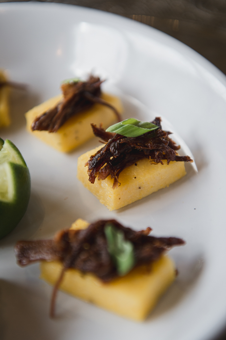Shredded braised beef on crispy polenta squares, garnished with sliced green onions.