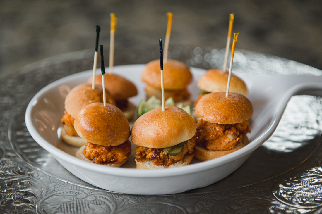 Mini fried chicken sliders with pickles, served on a white platter with toothpicks.