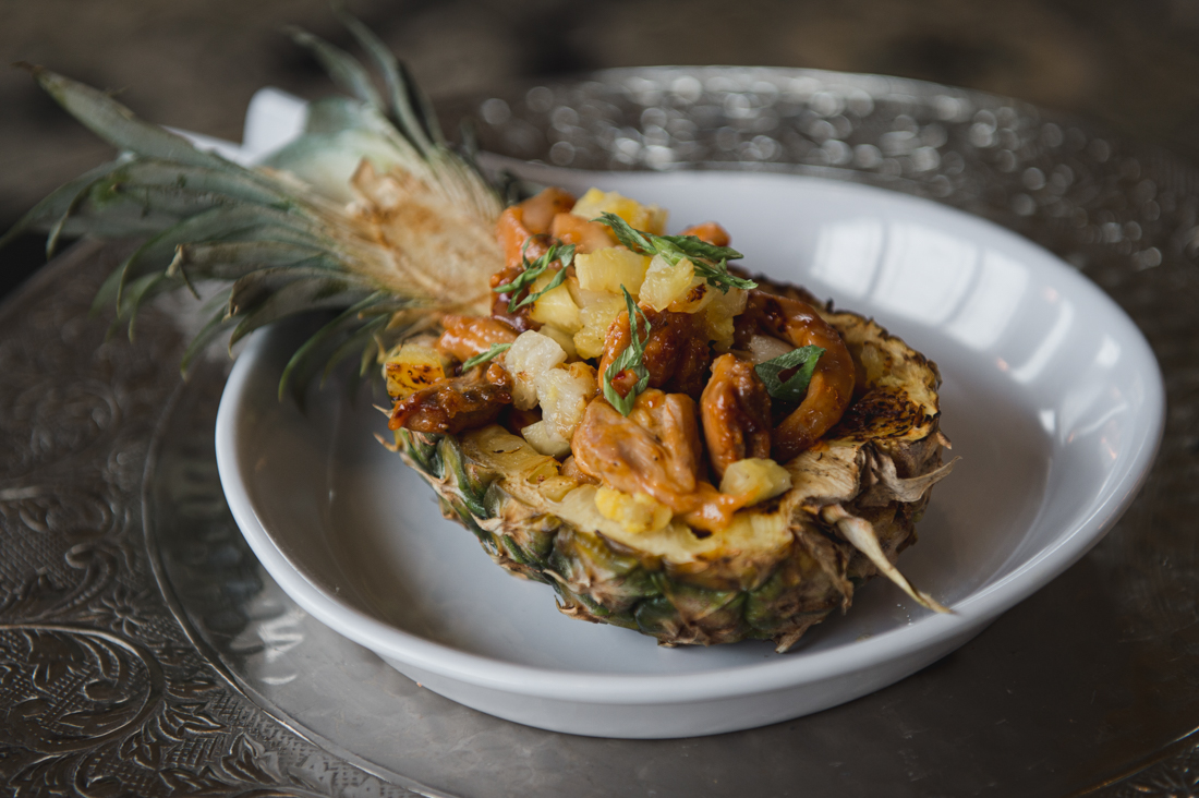 Sweet and sour chicken served inside a halved pineapple boat, garnished with fresh herbs.