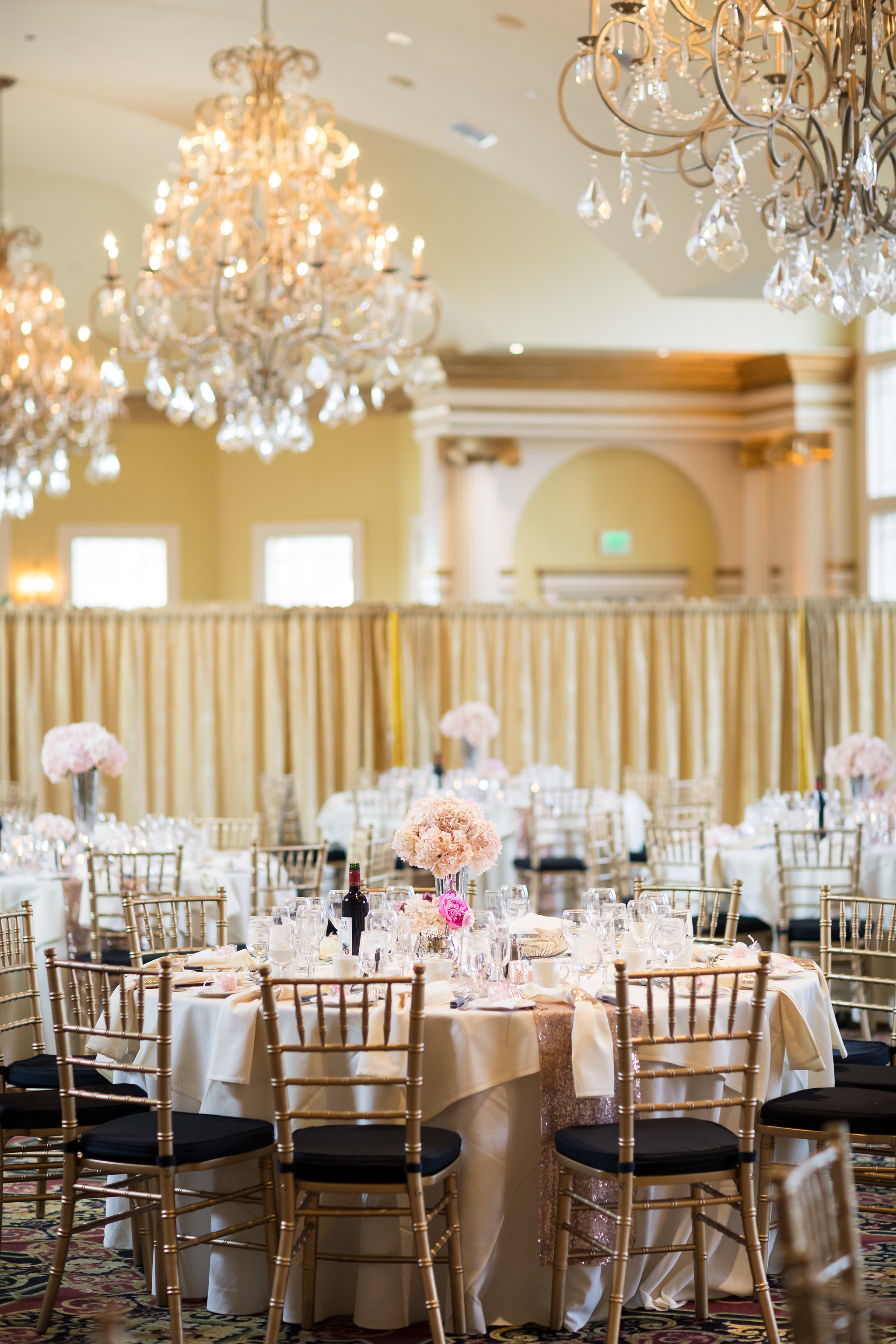 Elegant wedding reception ballroom with round tables, gold chairs, and crystal chandeliers.