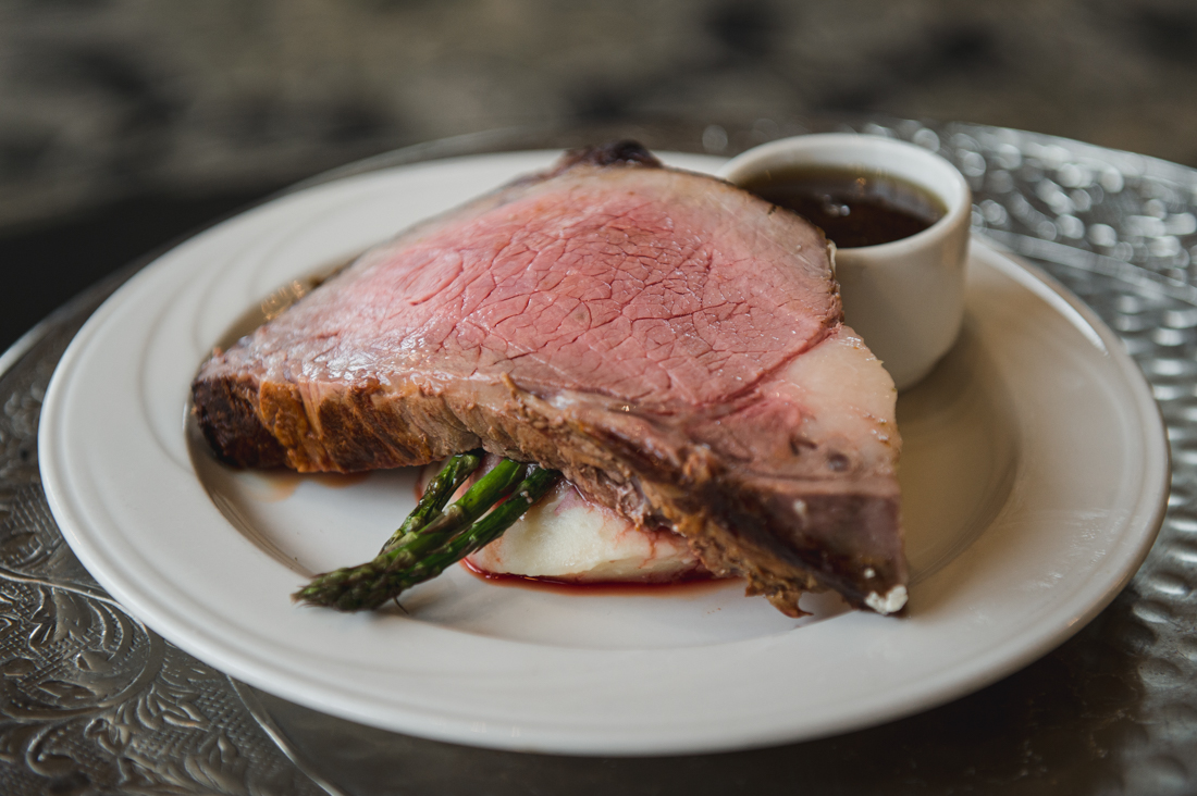 Prime rib served over mashed potatoes and asparagus with a small dish of au jus.