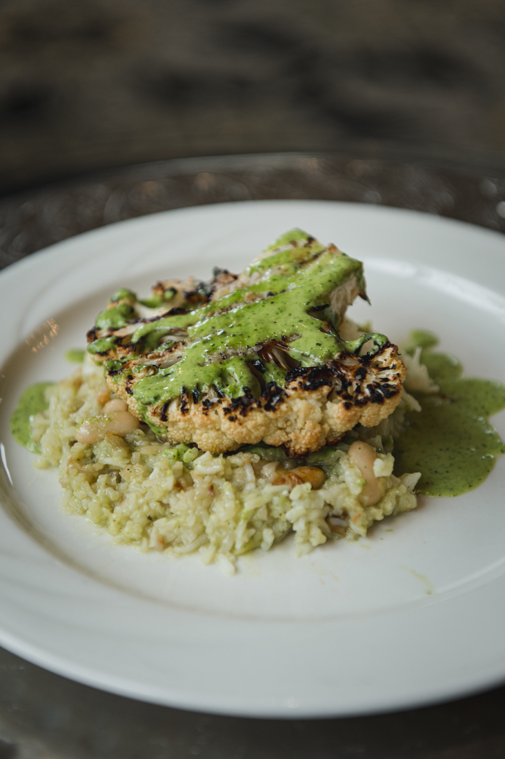 Roasted cauliflower steak drizzled with a vibrant green herb sauce, served over a bed of risotto.