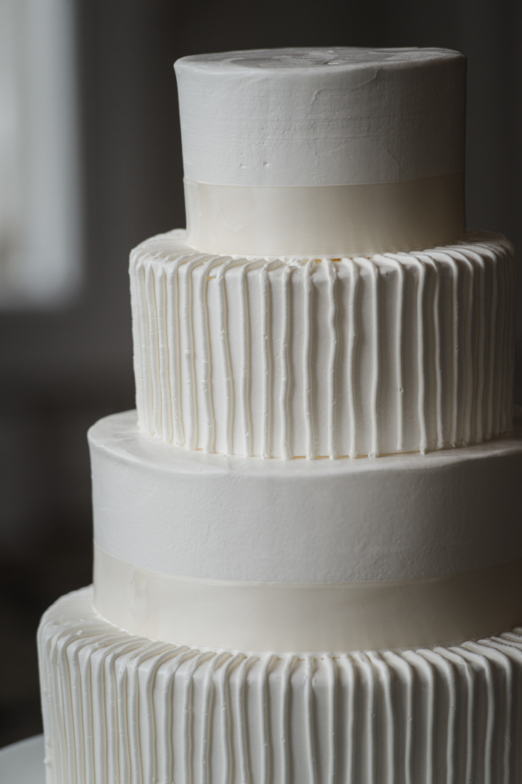 Four-tier white wedding cake with alternating smooth ribbon layers and vertical buttercream piping.
