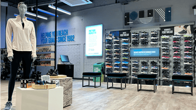 Modern running shoe store display with a mannequin, wide selection of supportive running shoes, and digital signage promoting fit and footwear advice.