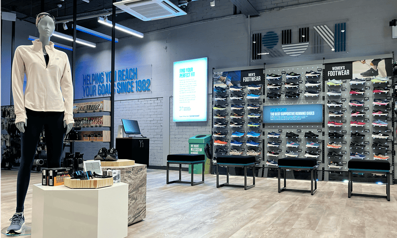 Modern running shoe store display with a mannequin, wide selection of supportive running shoes, and digital signage promoting fit and footwear advice.