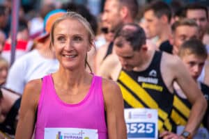Running Insights, marathon runner smiling at start line with other participants, summer race event, athletic apparel, focus on endurance, speed, motivation, health and fitness, UK marathon scene, competitive running.