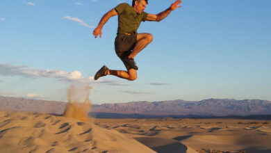 High-energy man jumping over desert sand dunes during daytime, showcasing agility and dynamic movement in a challenging outdoor environment.