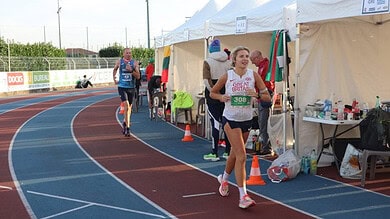 Competitive female runner smiling at a track event in Great Britain, close to the finish line, during a marathon or race with support tents in the background, highlighting endurance and athletic achievement.