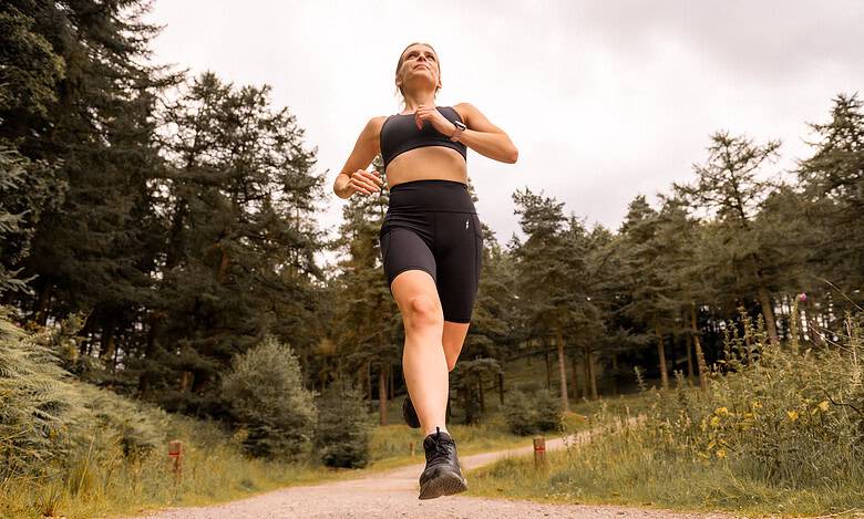 Female runner in black sportswear running on forest trail, outdoor running, fitness training, trail running, athletic performance, endurance, healthy lifestyle, Running Insights.