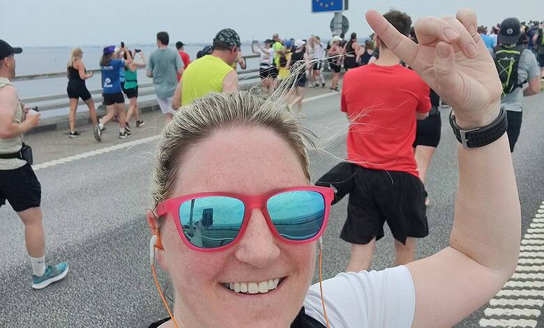 Bright smiling female runner taking a selfie during a marathon or outdoor running event on a scenic coastal route with a large crowd of participants, reflecting running insights and marathon training outdoors.