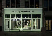 Exterior of House of Sportsshoes storefront at night with illuminated sign and mannequins inside.