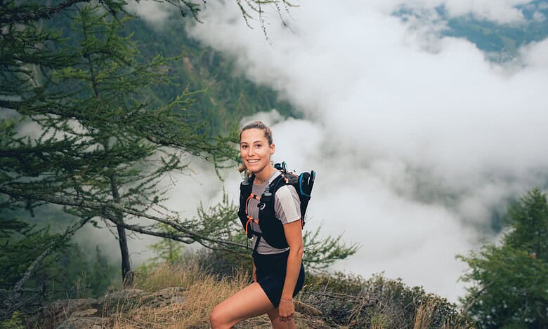 An adventurous woman trail running through lush forest terrain, showcasing ASICS trail shoes designed for outdoor running and exploration.